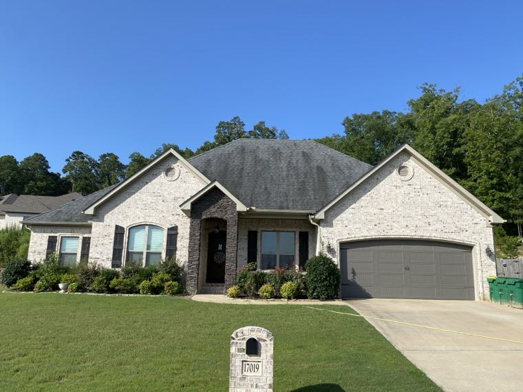 Brick home with dark algae streaking across the roof before cleaning
